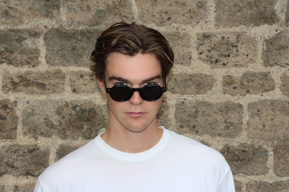 Person wearing sunglasses and a white shirt against a brick wall